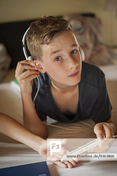Porträt eines Jungen  der auf dem Bett liegt und Musik mit Kopfhörern hört.