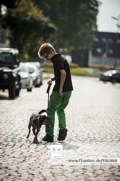 Junge  der mit seinem Hund auf einer Straße spazieren geht.