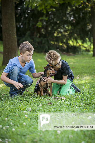 Zwei Jungen kauern mit ihrem Hund auf einer Wiese.