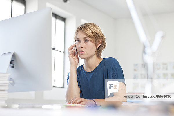 Porträt einer jungen Frau beim Telefonieren am Schreibtisch in einem Kreativbüro