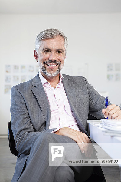 Porträt eines lächelnden Mannes an seinem Schreibtisch im Büro