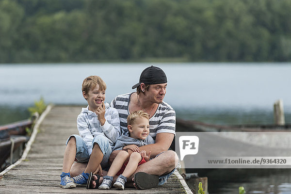 Germany  Rhineland-Palatinate  Laacher See  father sitting with two sons on jetty
