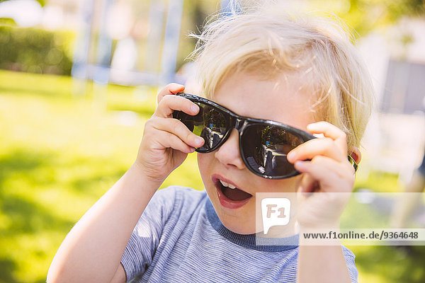Boy putting on giant black sunglasses in garden