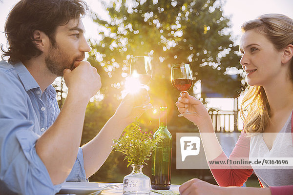 Couple clinking red wine glasses at table in evening light