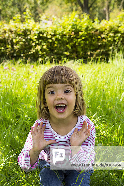 Porträt eines kleinen Mädchens  das auf einer Wiese mit verstreuten Früchten sitzt.