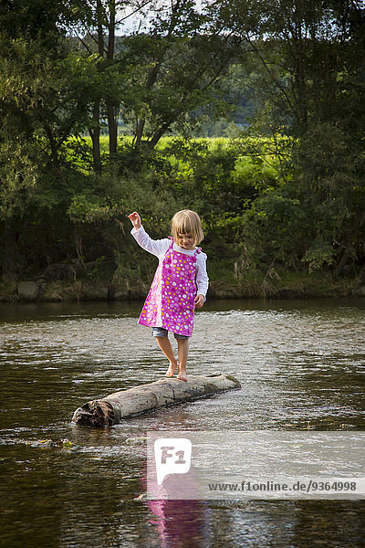 Kleines Mädchen  das auf einem Felsen in einem Fluss balanciert.