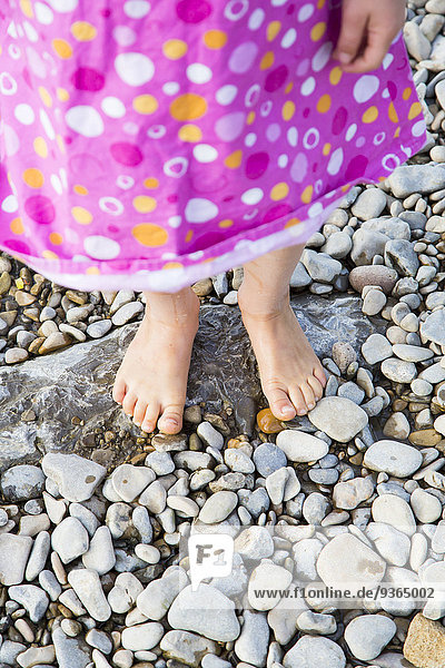 Füße des kleinen Mädchens auf Kieselsteinen am Flussufer stehend