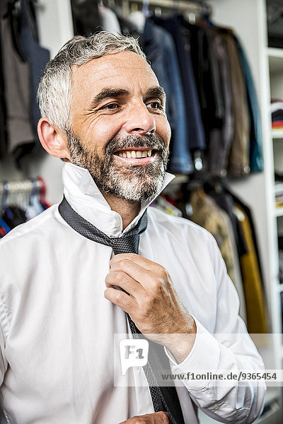 Portrait of smiling businessman binding tie at his walk-in closet