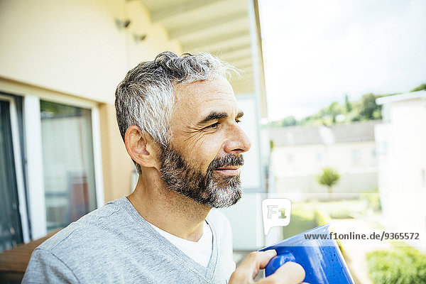 Portrait of smiling man relaxing with cup of coffee on his balcony