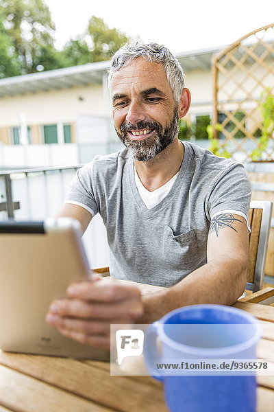 Porträt eines lächelnden Mannes  der auf seinem Balkon sitzt  mit einem digitalen Tablett.