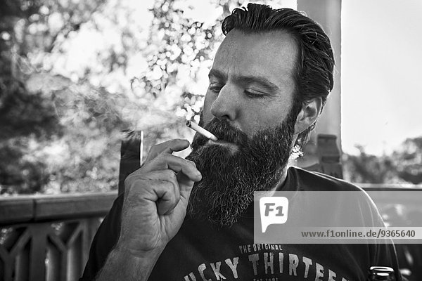Man with full beard smoking cigarette on porch