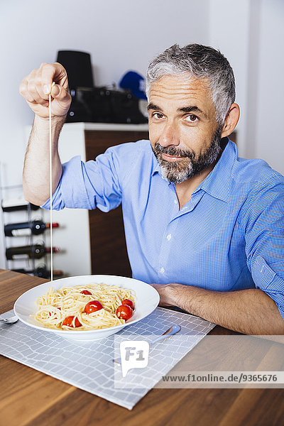 Porträt eines Mannes  der in seiner Küche Pasta isst.