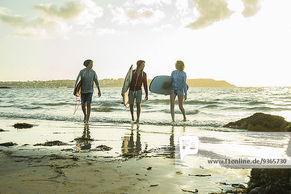 Drei Teenager mit Surfbrettern am Strand in der Abenddämmerung