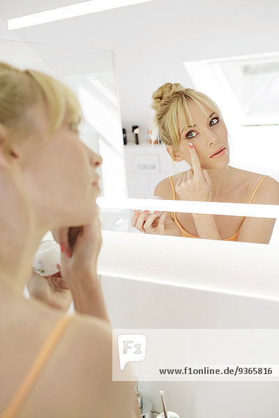 Frau betrachtet ihr Spiegelbild beim Auftragen der Gesichtscreme