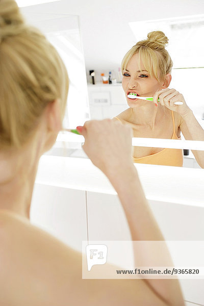 Frau schaut beim Zähneputzen auf ihr Spiegelbild
