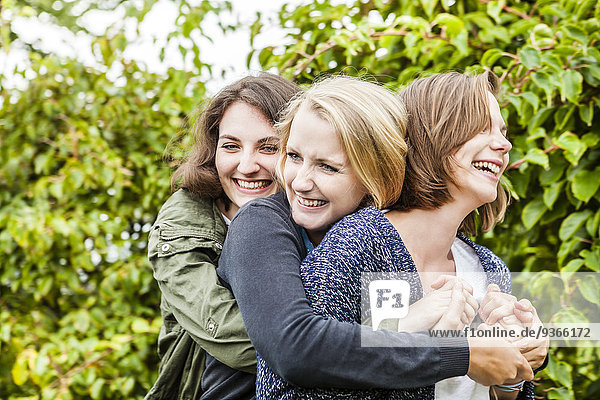 Drei Freundinnen umarmen sich im Garten