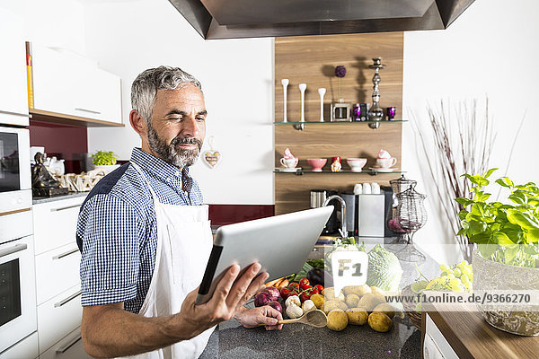 Österreich  Mann in der Küche mit digitalem Tablett  sucht Rezept