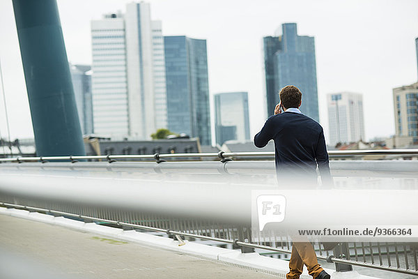 Deutschland  Hessen  Frankfurt  junger Geschäftsmann  der auf einer Brücke läuft und mit seinem Smartphone telefoniert.