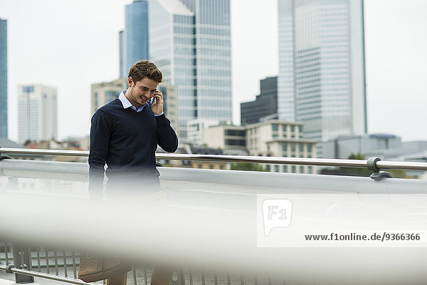Deutschland  Hessen  Frankfurt  junger Geschäftsmann  der auf einer Brücke läuft und mit seinem Smartphone telefoniert.