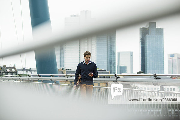 Deutschland  Hessen  Frankfurt  junger Geschäftsmann  der mit seinem Smartphone auf einer Brücke läuft.