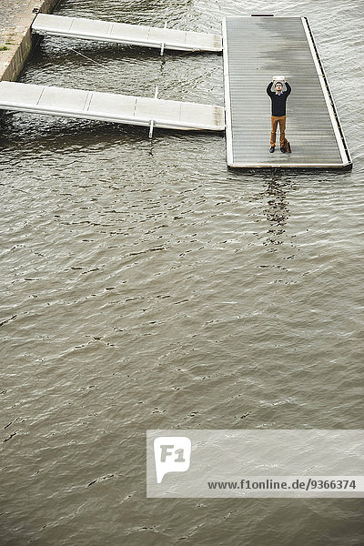Deutschland  Hessen  Frankfurt  junger Mann  der auf einem Steg steht und mit seinem digitalen Tablett einen Selfie mitnimmt.
