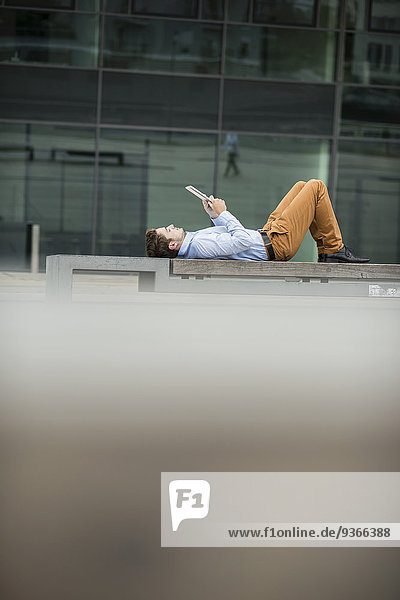 Deutschland  Hessen  Frankfurt  junger Mann auf dem Rücken liegend mit seinem digitalen Tablett