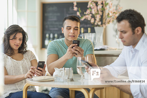Hispanic friends using cell phones in cafe
