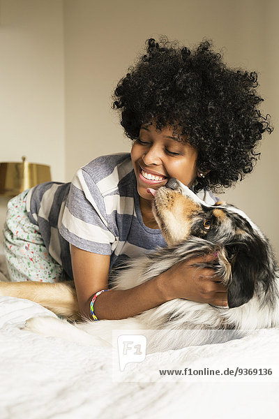 Mixed race woman playing with dog on bed