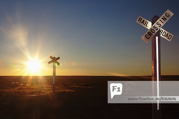 Railroad crossing sign on remote road at sunset