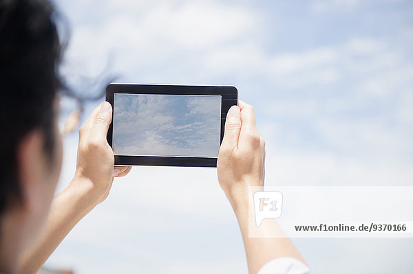 Close up of mixed race man photographing clouds with digital tablet