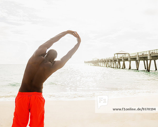 Mixed race man stretching on beach