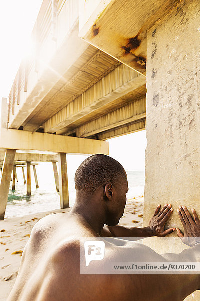 Mixed race man stretching under pier