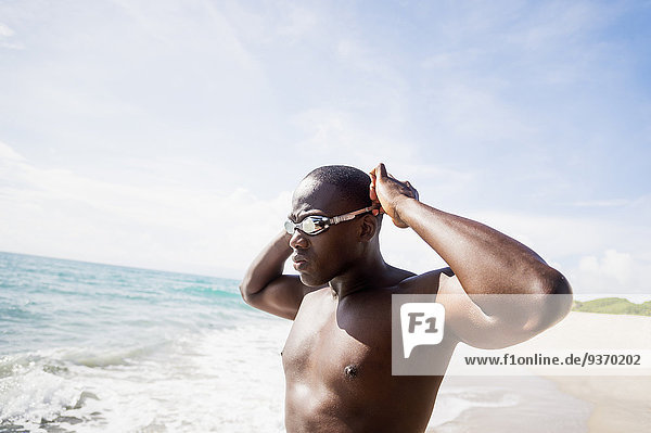 Mixed race swimmer putting on goggles at beach