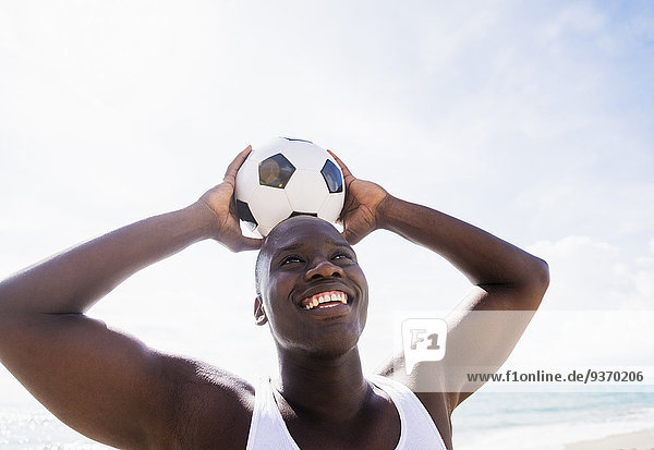 Mixed race man holding soccer ball on beach
