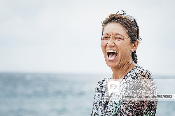 Asian woman laughing near ocean