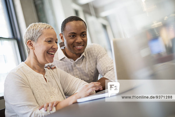 Büroalltag. Zwei Menschen  ein Mann und eine Frau  die auf einen Laptop-Bildschirm schauen und lachen.