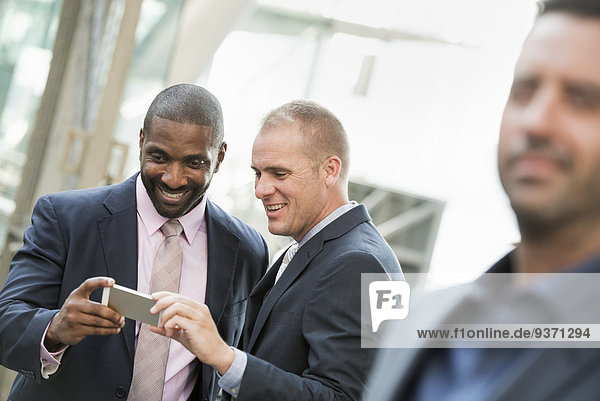 Two businessmen checking a phone and laughing  one man in the fore.