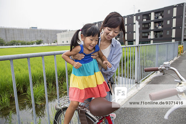 Eine Mutter hebt ihre Tochter auf ein Fahrrad.