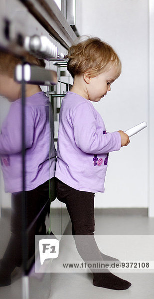 Mädchen steht mit einem schnurlosen Telefon am Elektroherd