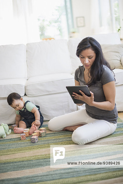 Mother using tablet pc while her son (6-11 months) playing with building blocks