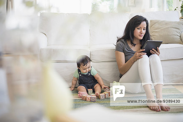 Mother using tablet pc while her son (6-11 months) playing with building blocks