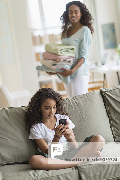 Girl (8-9) text messaging on sofa  mother in background