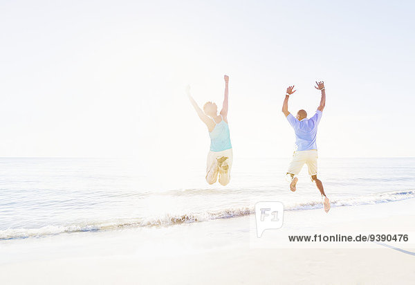 Mature couple jumping in sea with arms raised