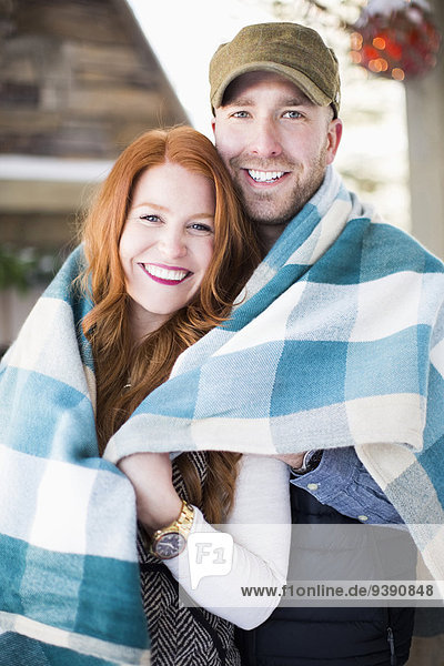 Portrait of mid adult couple wrapped in checked blanket