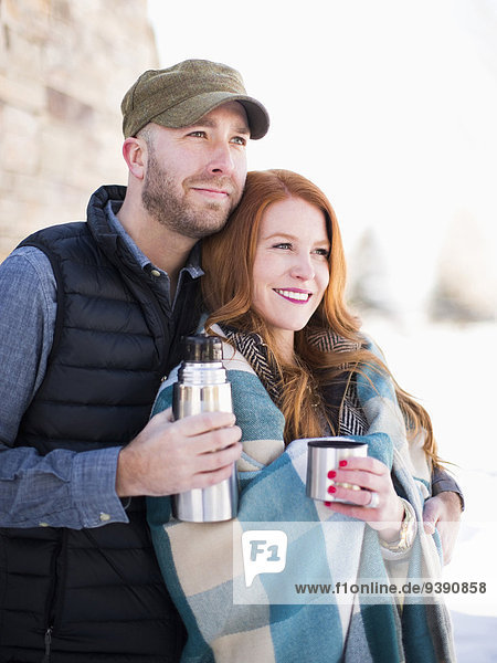 Mid adult couple having drink from vacuum flask  looking away