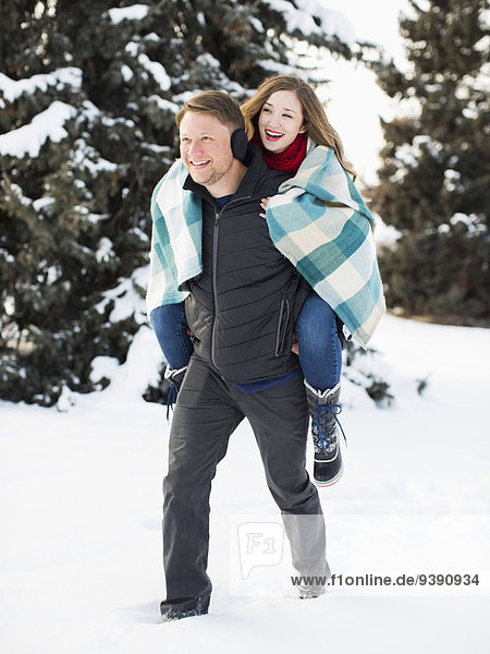 Man giving woman piggyback ride in winter forest