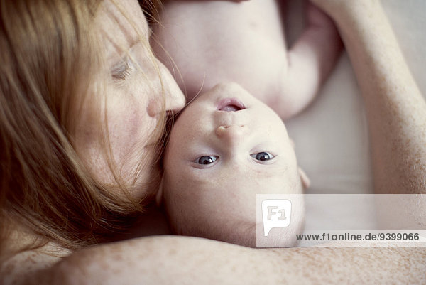 Mutter legt sich hin  küsst die Wange des Babys  Blick nach oben