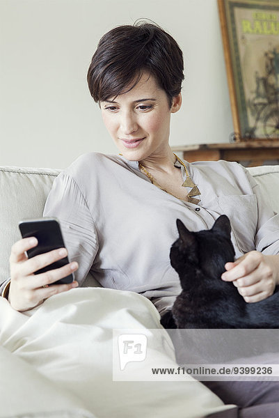 Frau auf dem Sofa sitzend mit Katze auf dem Schoß  mit Smartphone