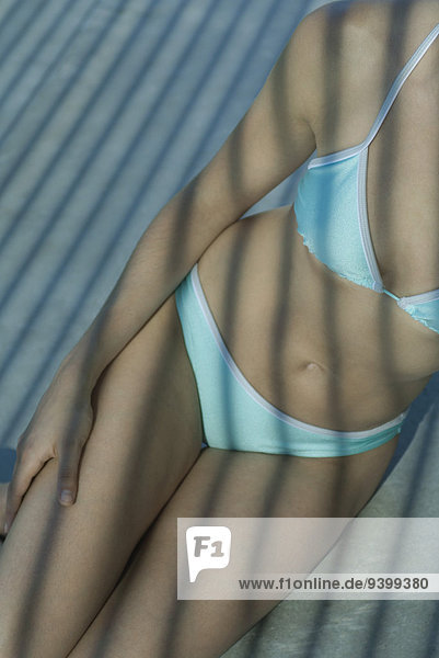 Frau im Bikini sitzend im Schatten  beschnitten