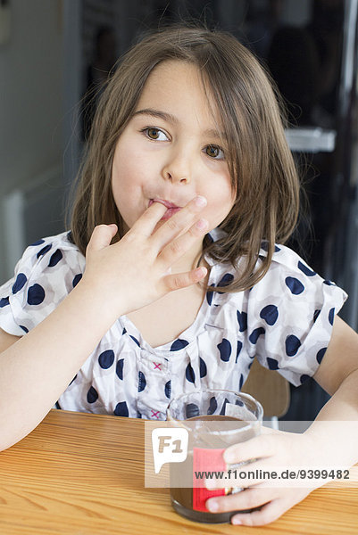 Kleines Mädchen isst Schokoladensauce aus einem Glas mit den Fingern